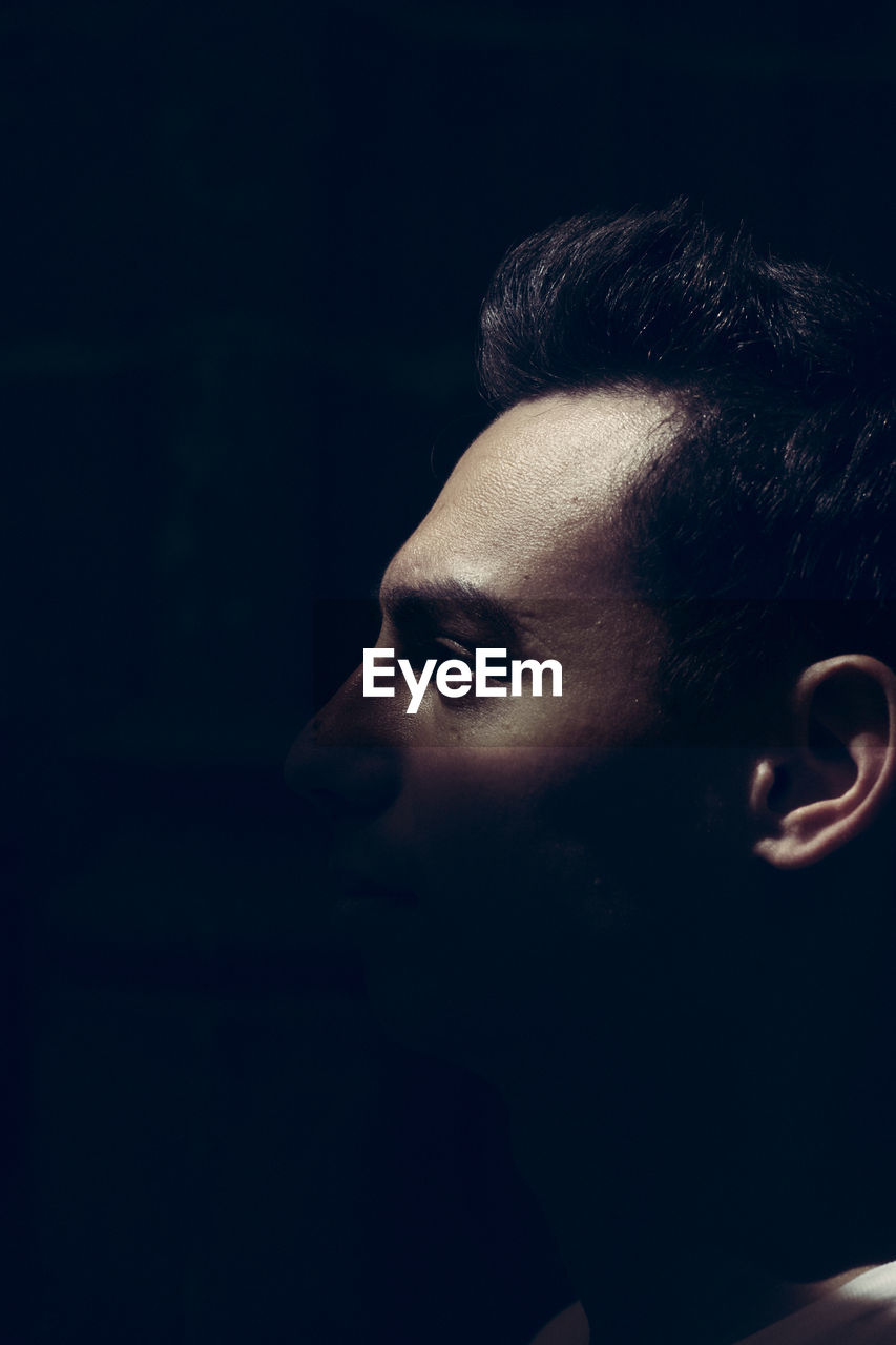 Close-up of young man looking away against black background