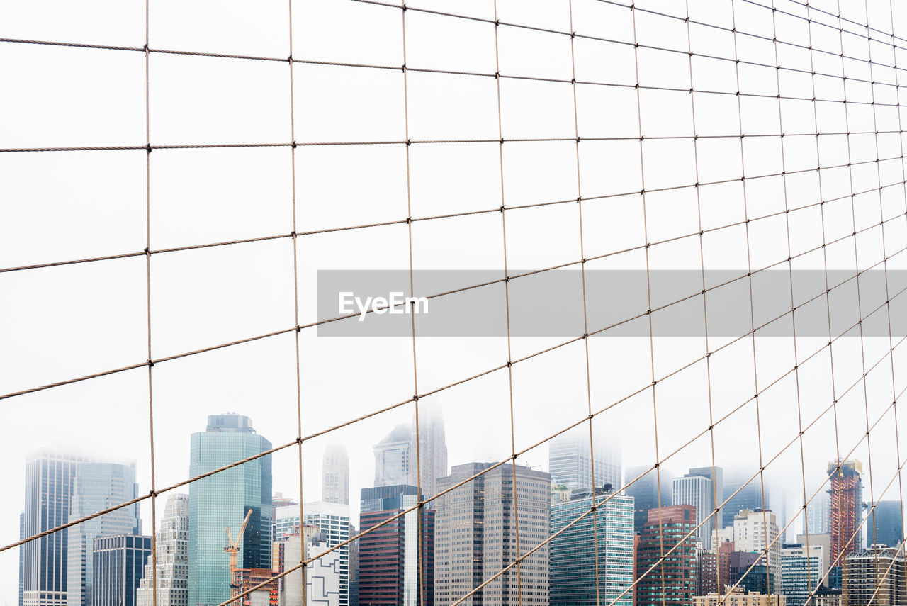 Low angle view of buildings seen through fence against sky