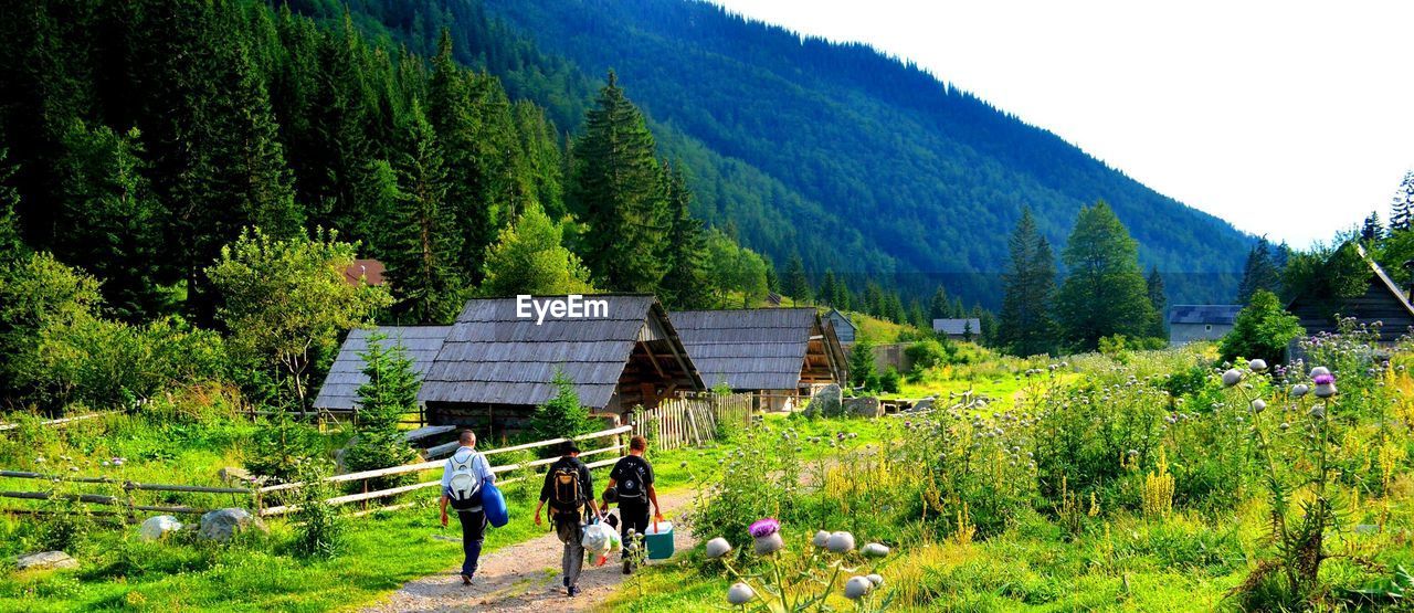 Panoramic shot of men walking on grassy field by mountains against clear sky