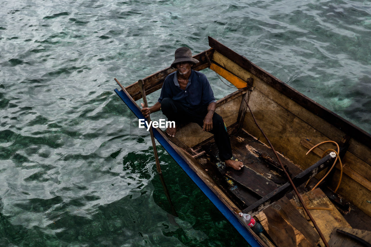 HIGH ANGLE VIEW OF MAN SITTING ON BOAT AT SEA
