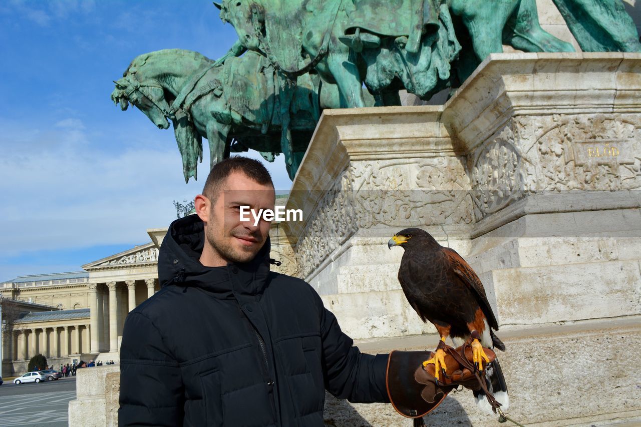 Portrait of smiling man holding bird in city