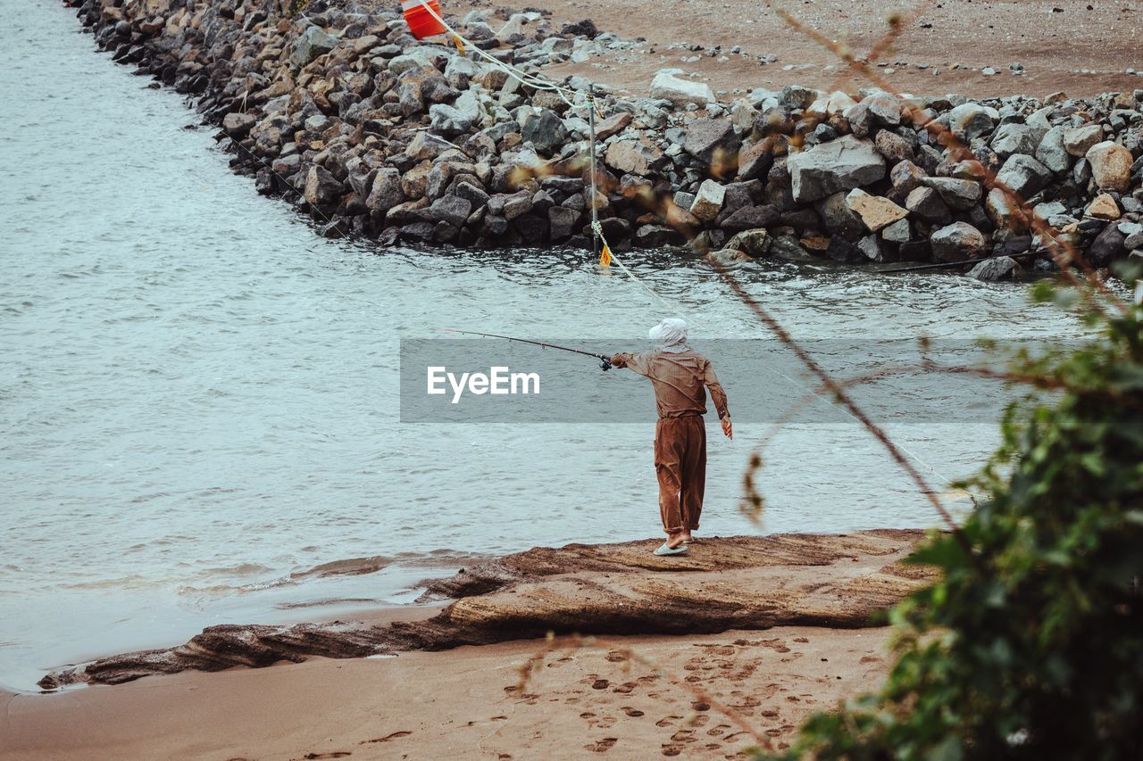 Rear view of fisherman fishing while standing on shore