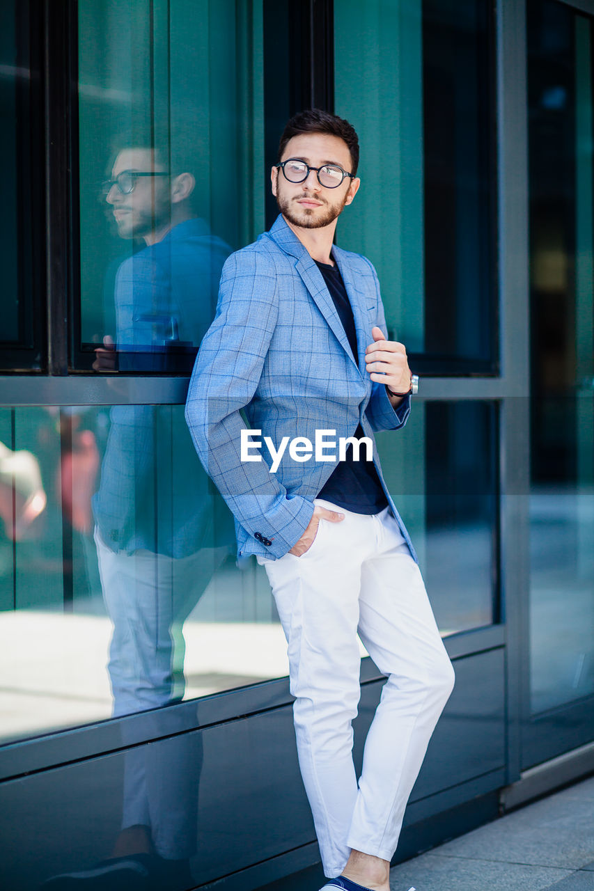 Full length portrait of young man leaning on glass wall