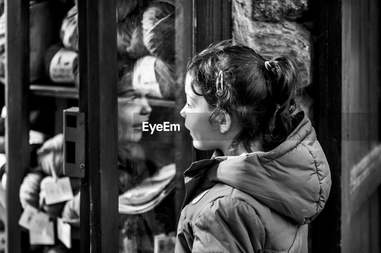 Side view of girl looking through window glass at store