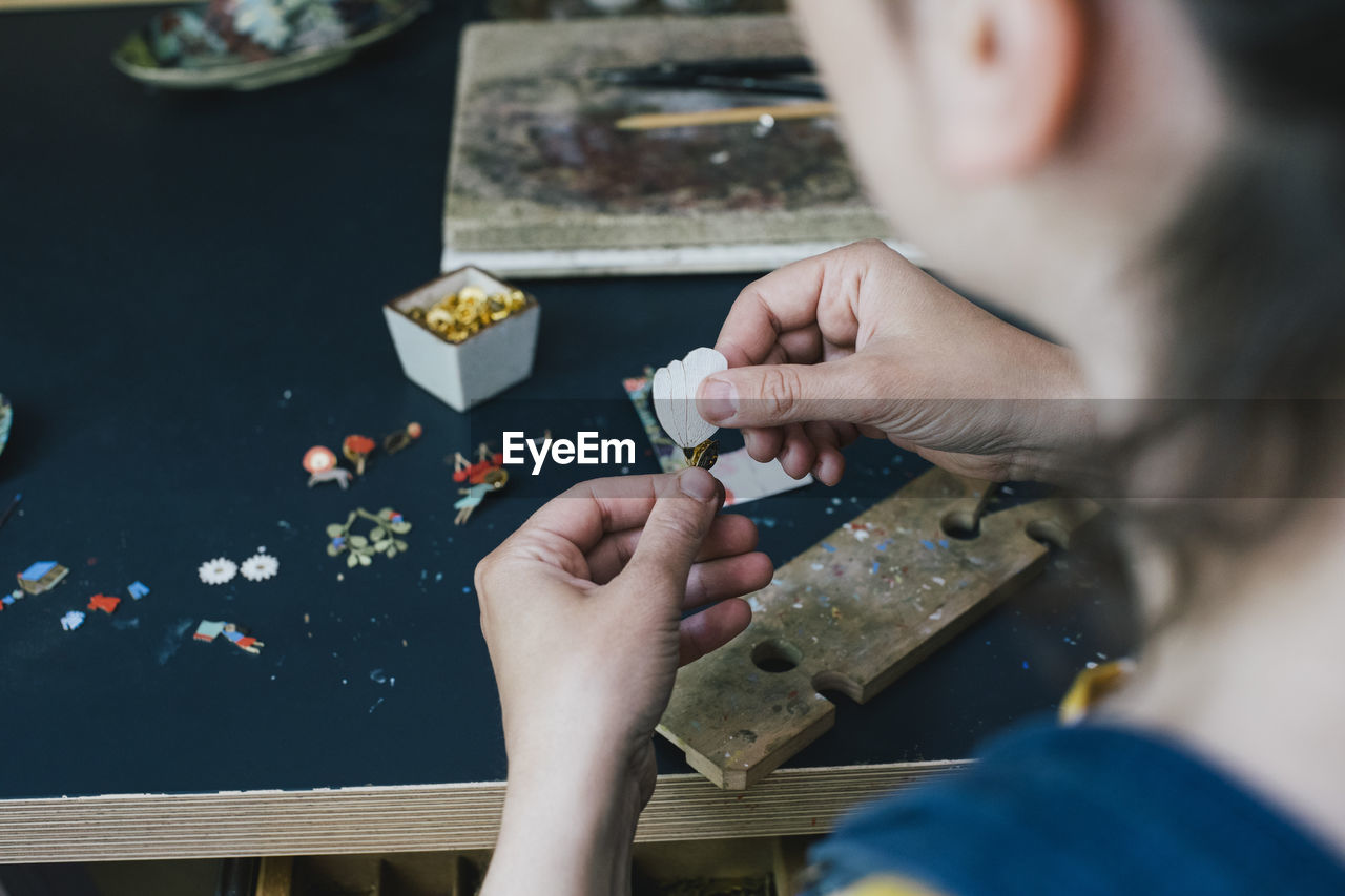 Hands of female craftsperson making jewelry on workbench