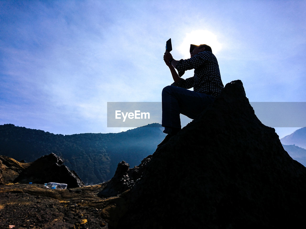 Man photographing on rock by mountains against sky