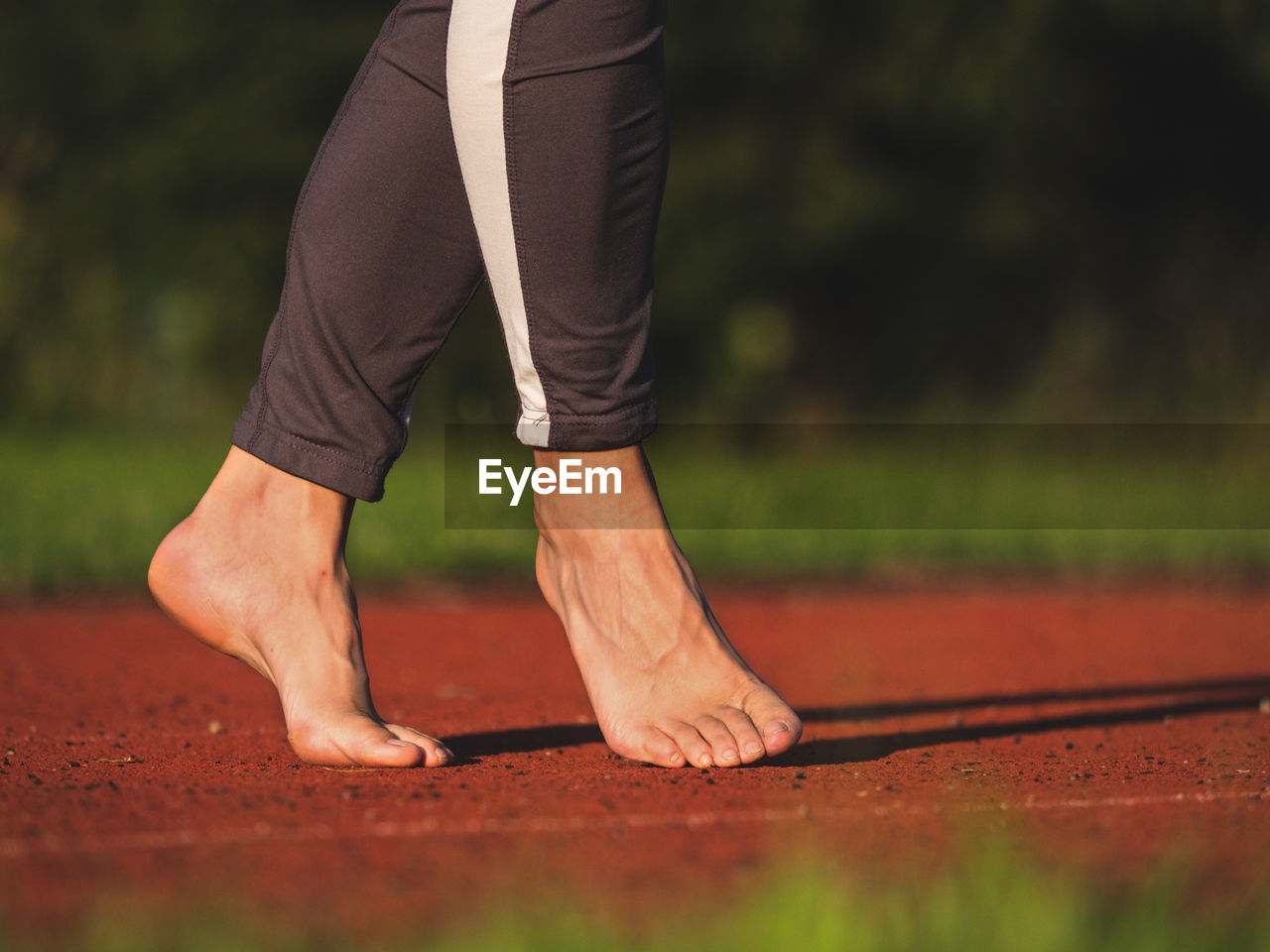 Barefoot woman walks on tiptoe, stretching tendons and ankles on red running track in long leggings