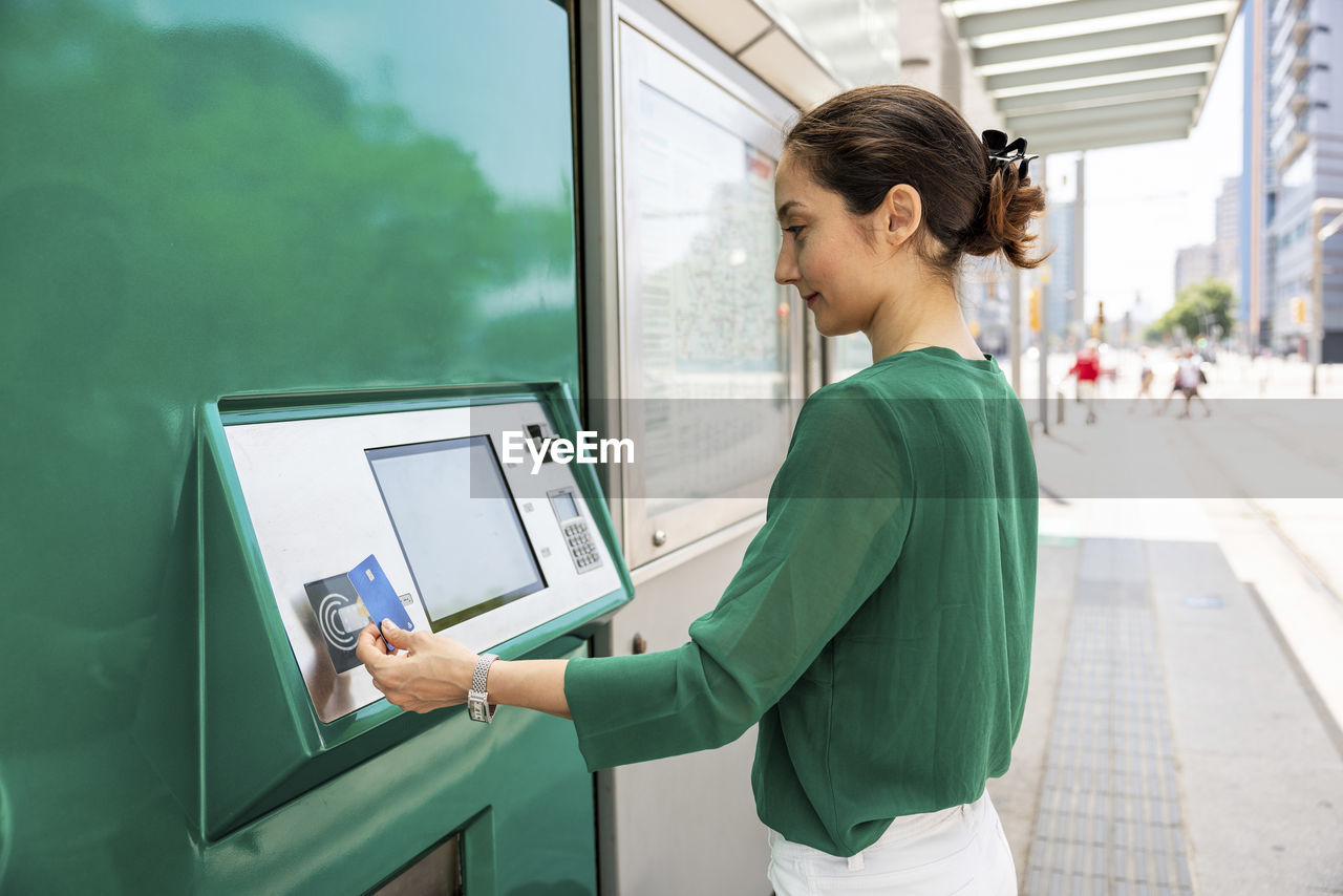 Smiling woman operating ticket machine with credit card at tram stop