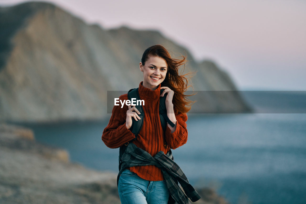 PORTRAIT OF SMILING YOUNG WOMAN STANDING OUTDOORS