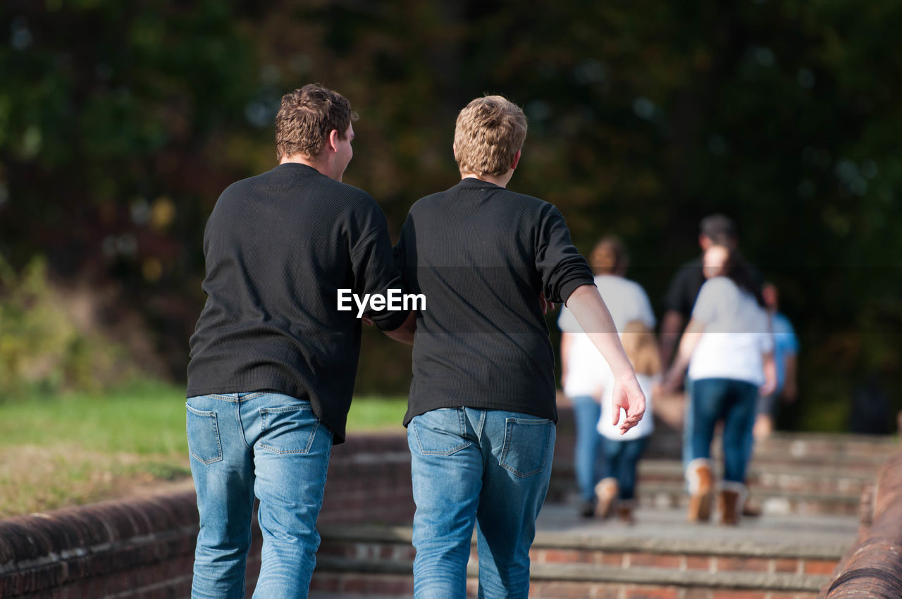 REAR VIEW OF TWO PEOPLE WALKING OUTDOORS