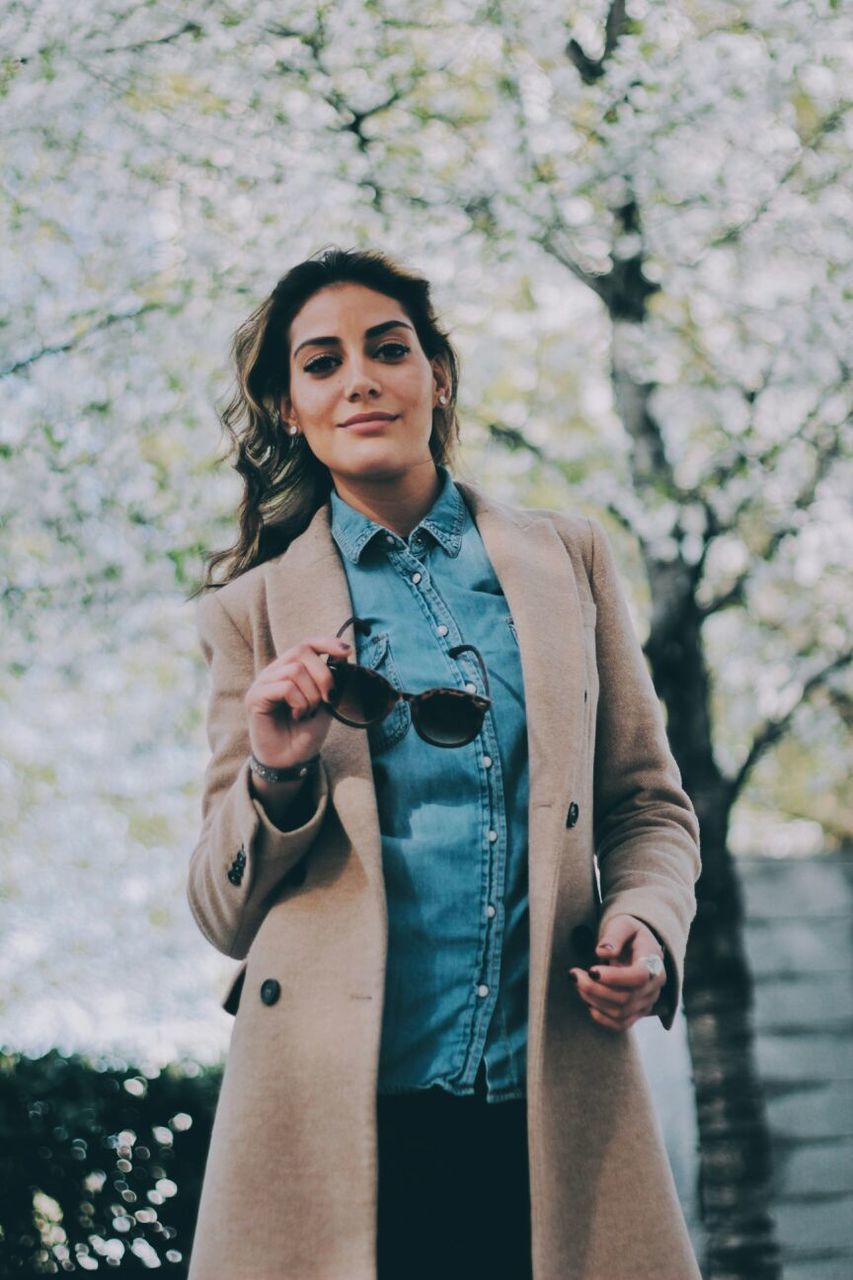 PORTRAIT OF HAPPY YOUNG WOMAN STANDING AGAINST TREE