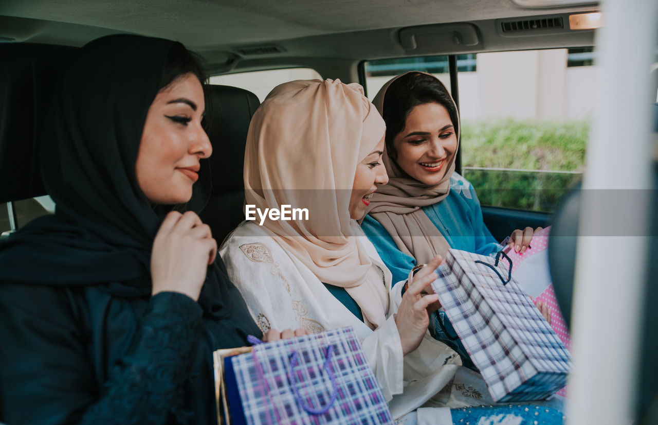 Cheerful women wearing hijab sitting in car with shopping bags