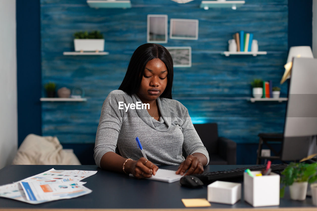 young woman using mobile phone while sitting on table in office