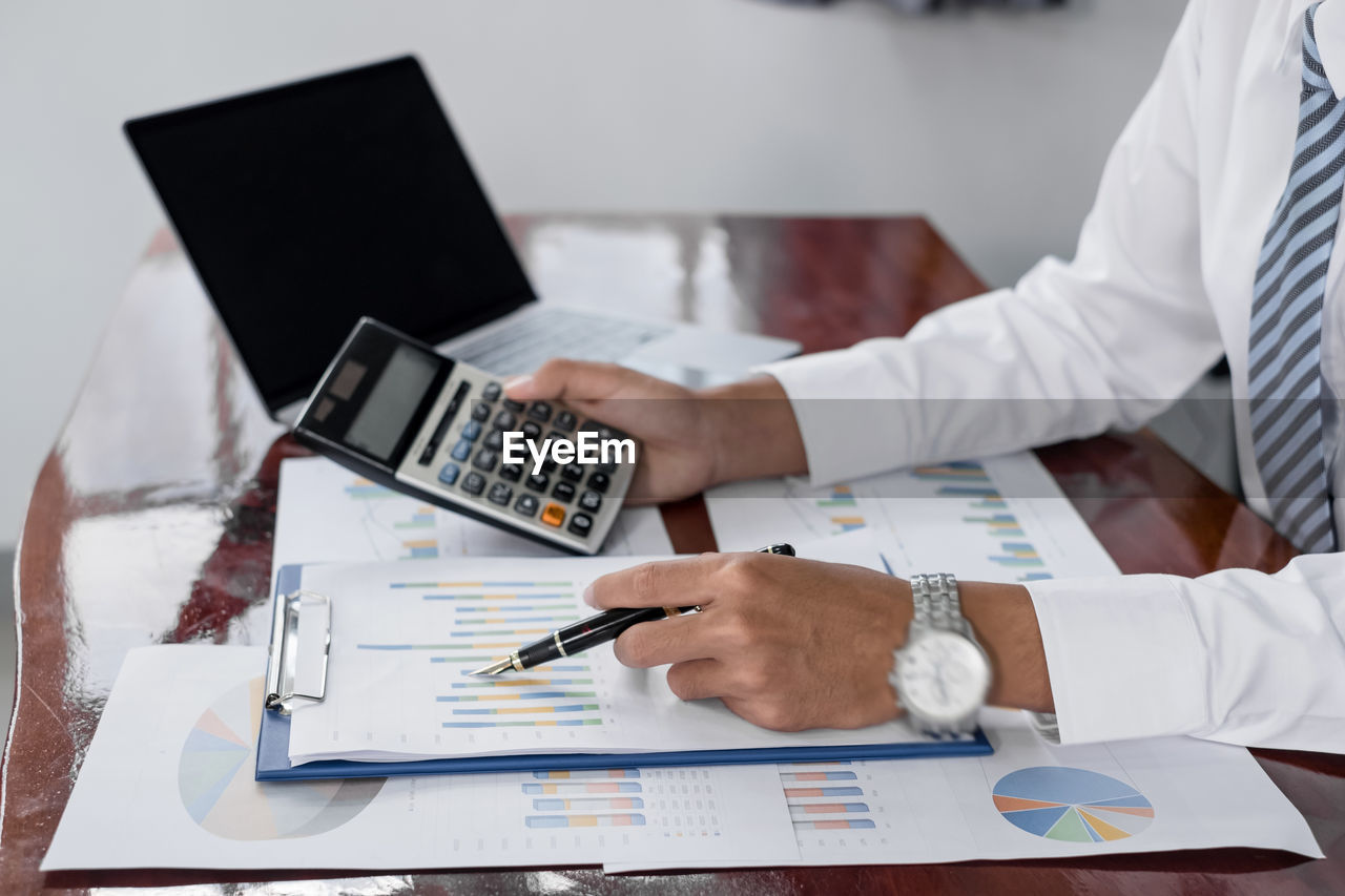 Midsection of businessman using calculator on table