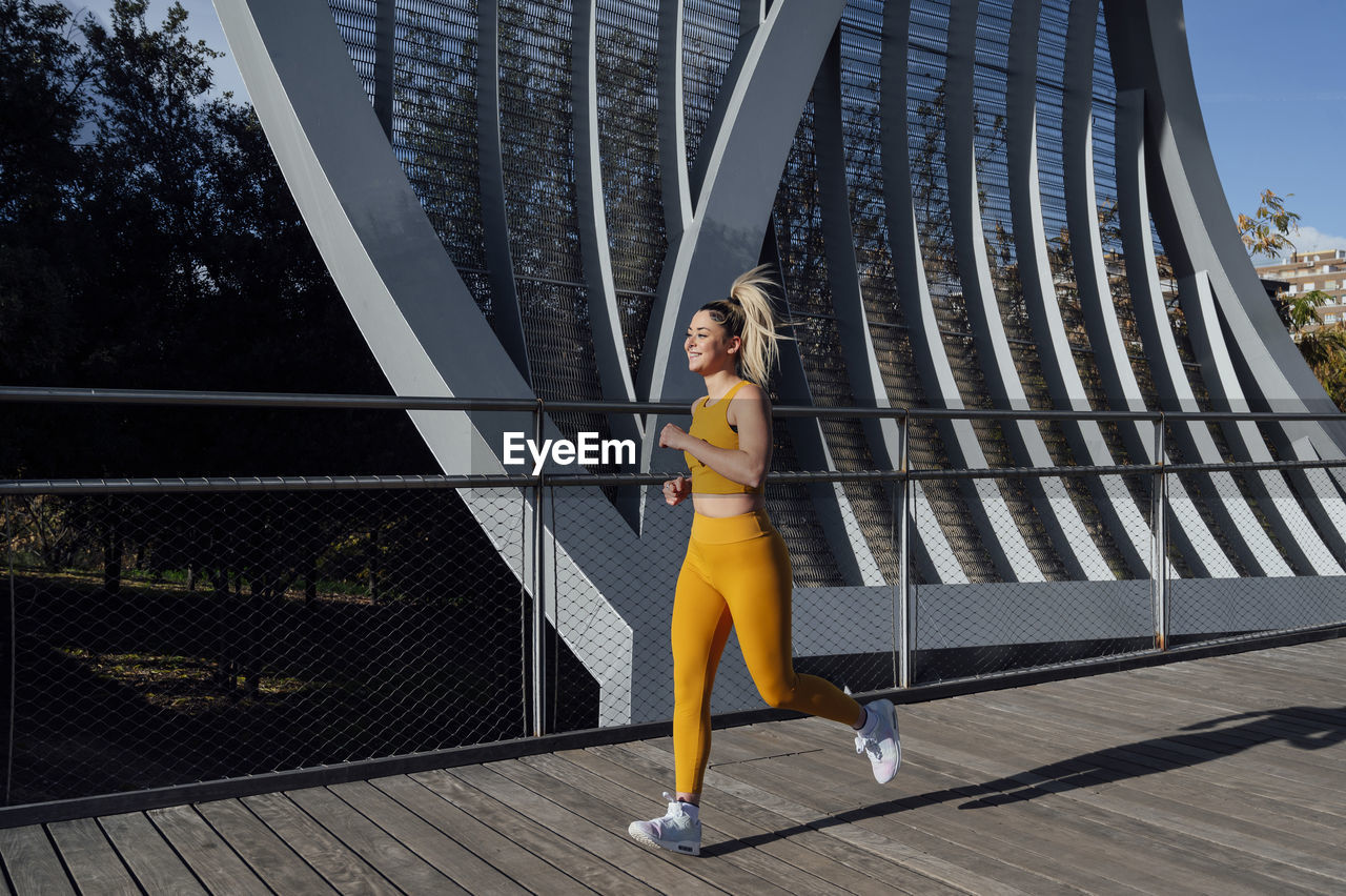 Smiling young athlete jogging on footbridge