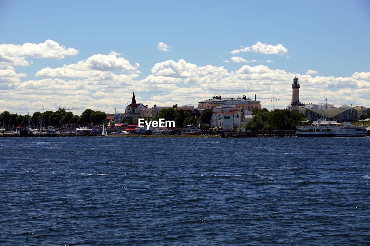 Buildings at waterfront against cloudy sky