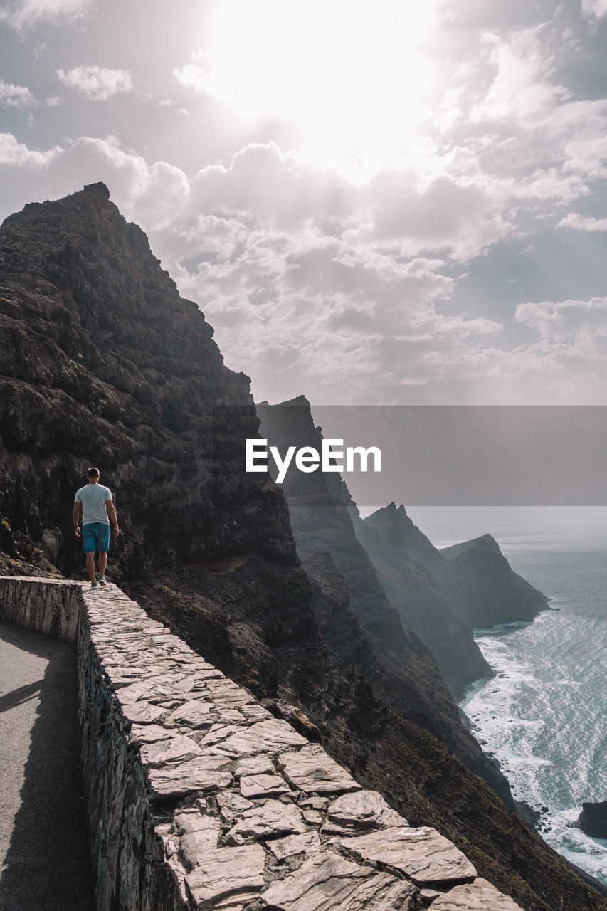 Rear view of man walking on retaining wall against mountain range