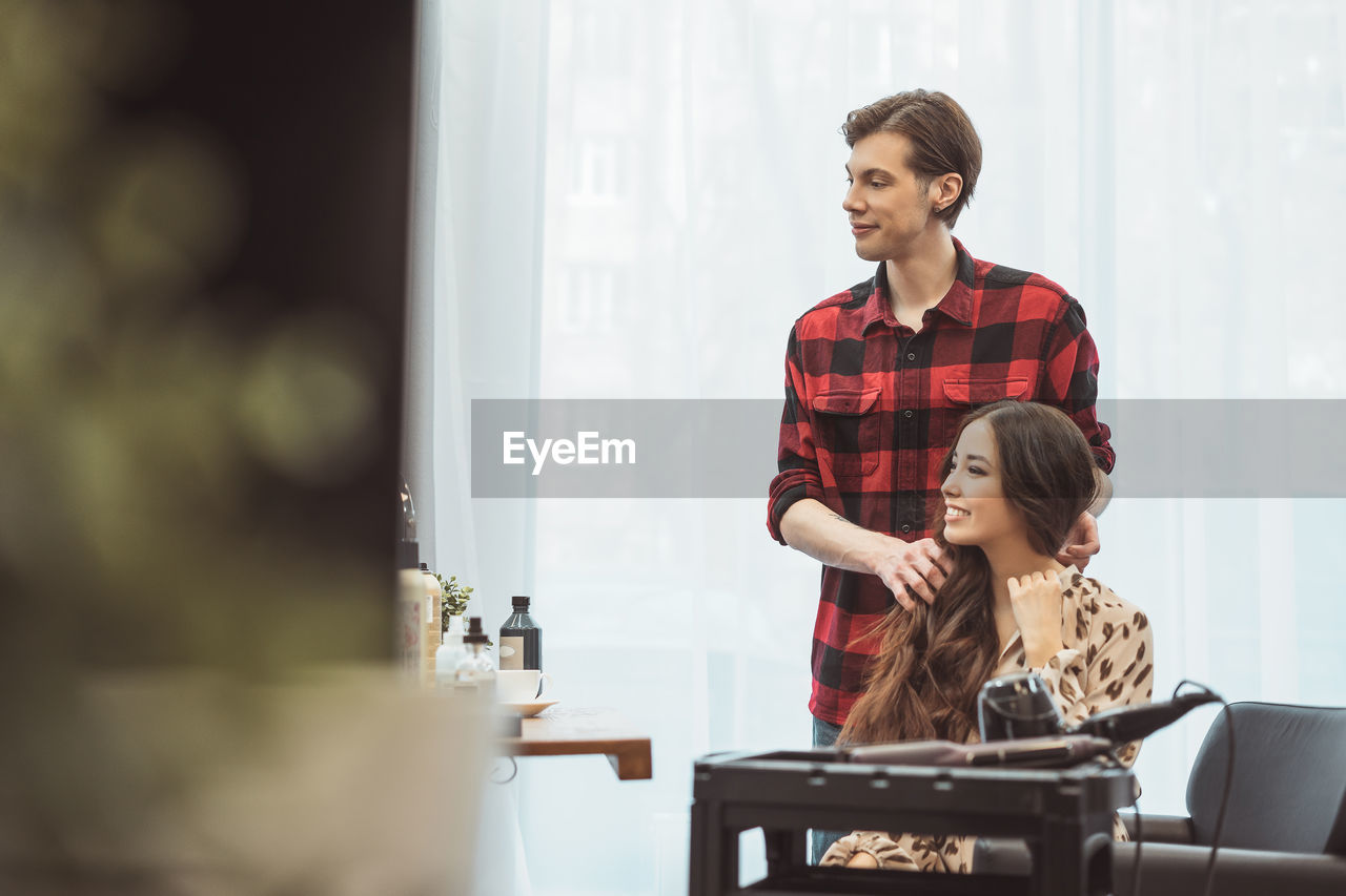 Stylist barber styling long hair for beautiful asian young woman in beauty salon, working moment