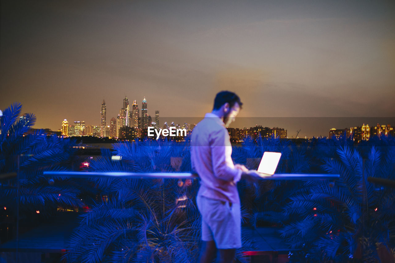 Man using laptop on terrace, cityscape on background