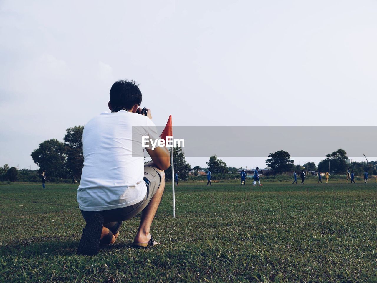 Man photographing while crouching on field against clear sky