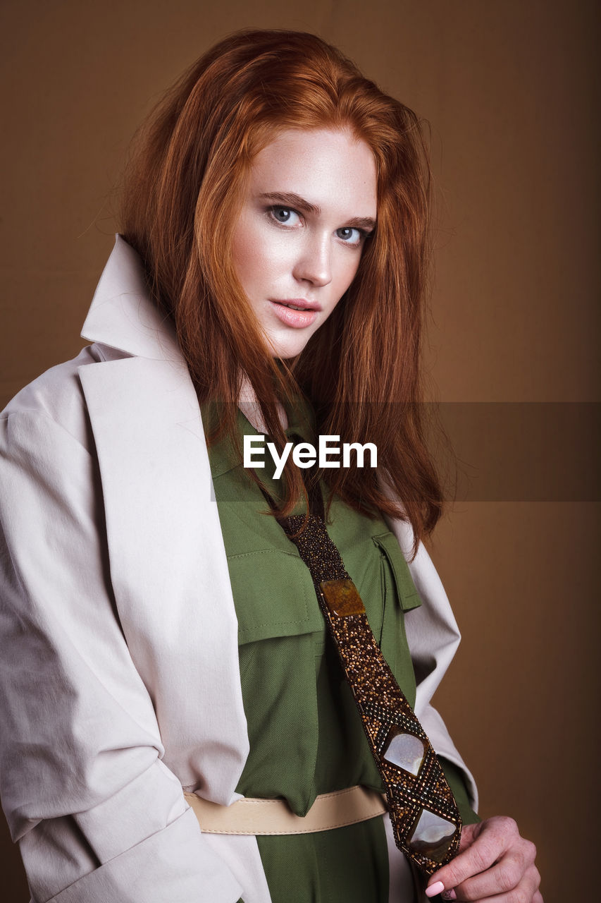 Portrait of young woman standing against brown background