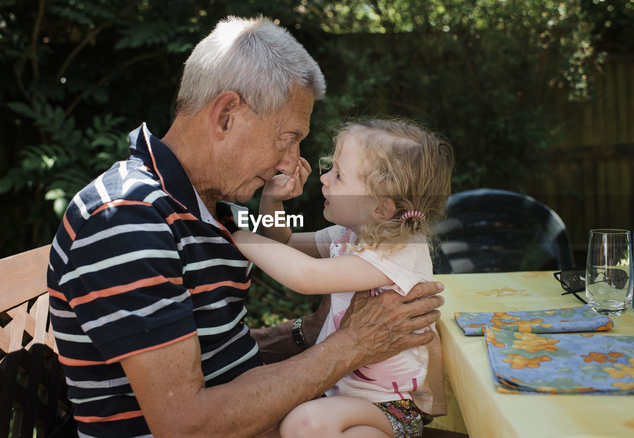 Side view of granddaughter touching grandfather's nose while sitting in yard