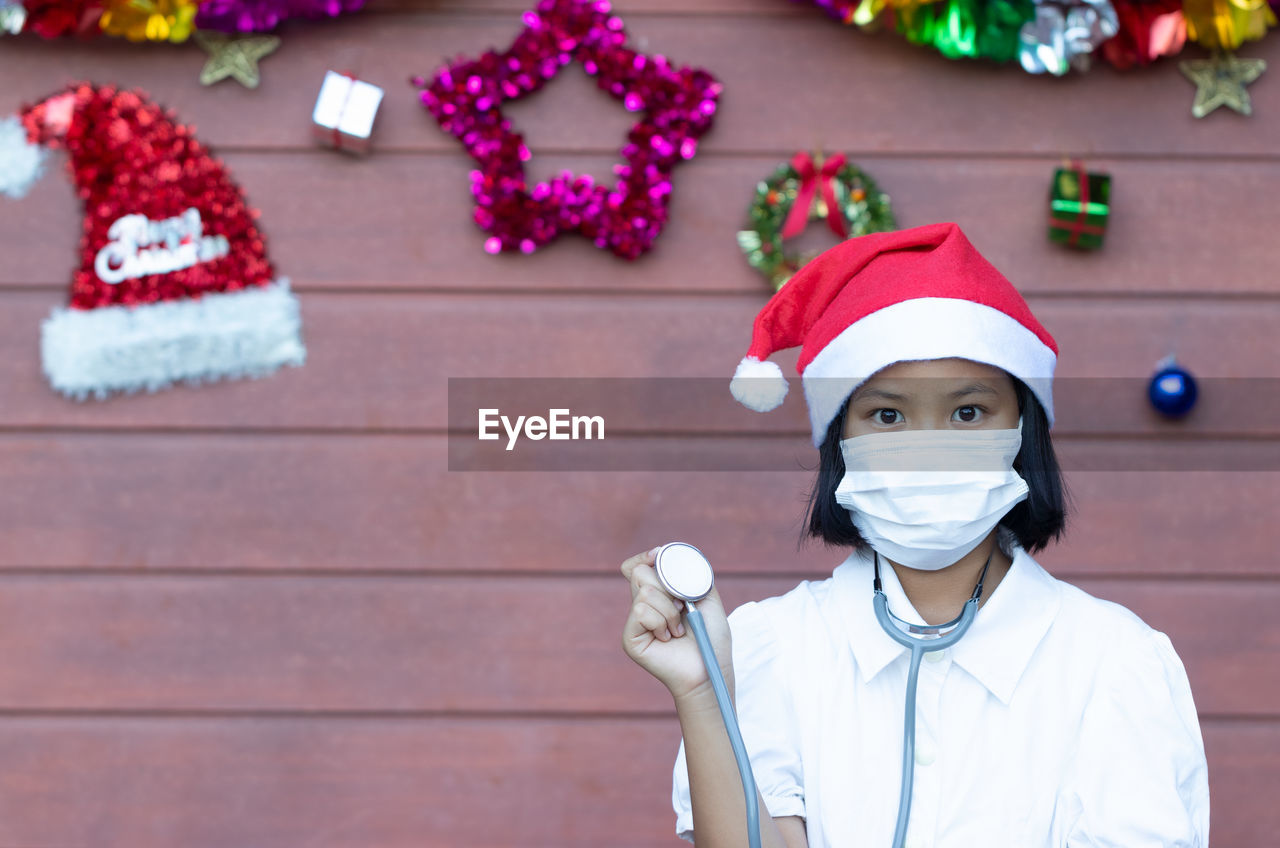 Portrait of girl wearing lab coat while standing against christmas decorations on wall