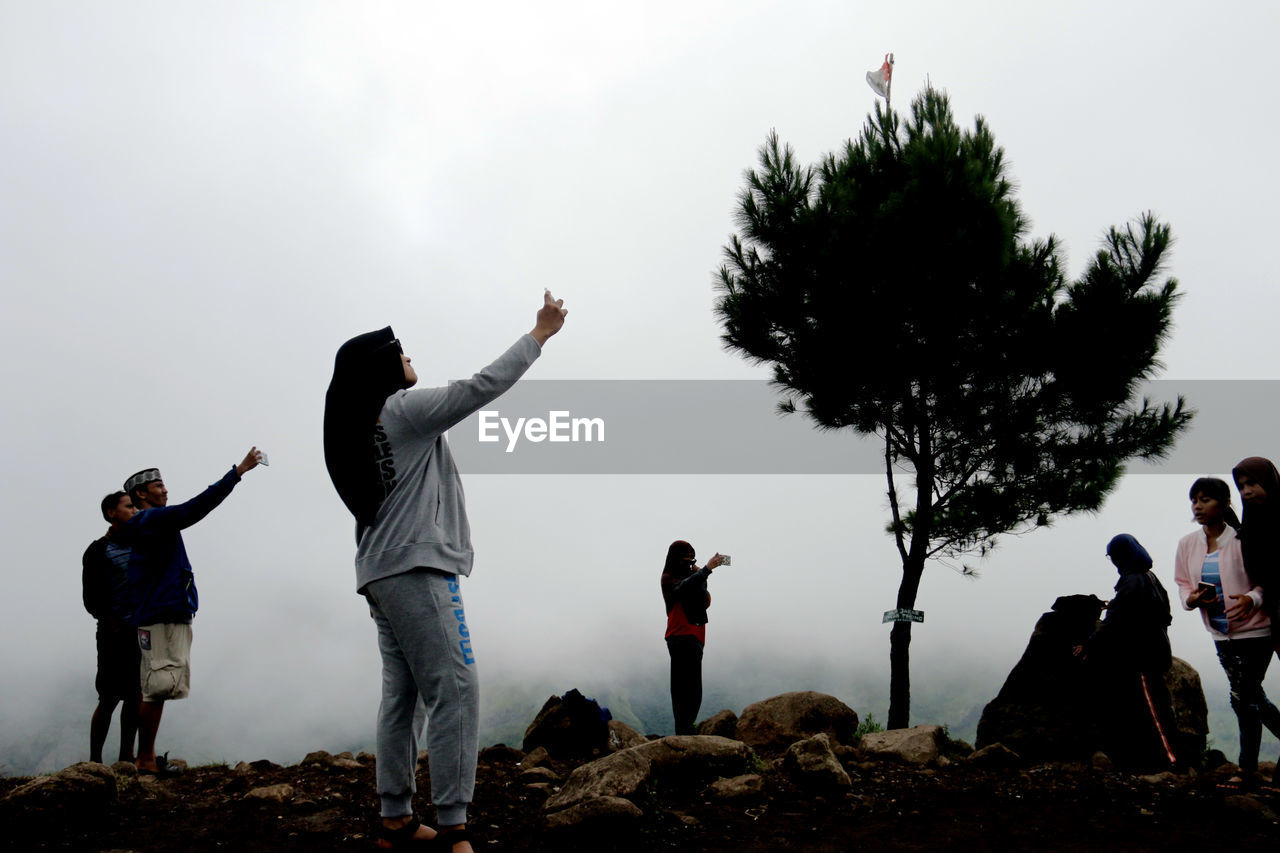 PEOPLE STANDING ON CACTUS AGAINST SKY