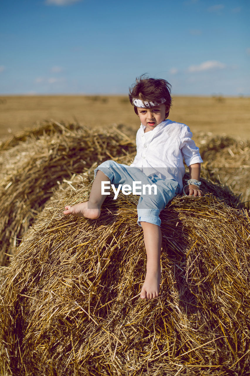 Boy child in bandana and white shirt sitting on a bale of hay in the summer