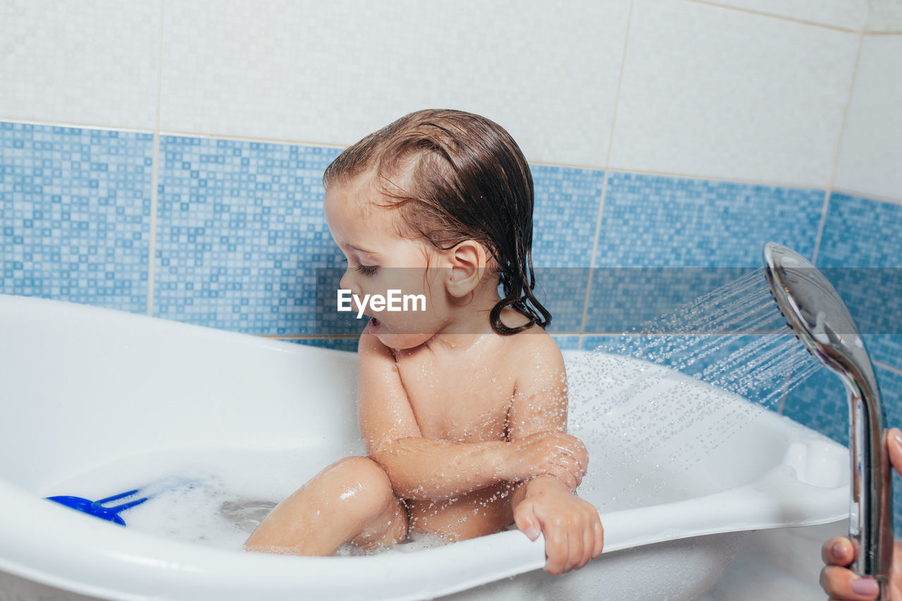 Cropped hand of mother spraying water on daughter in bathroom