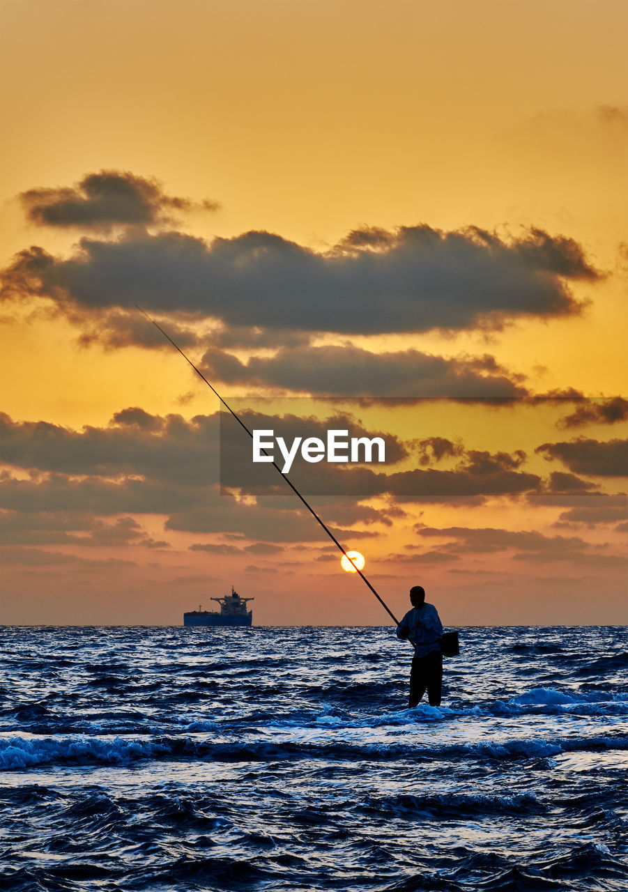 Silhouette man fishing in sea against sky during sunset