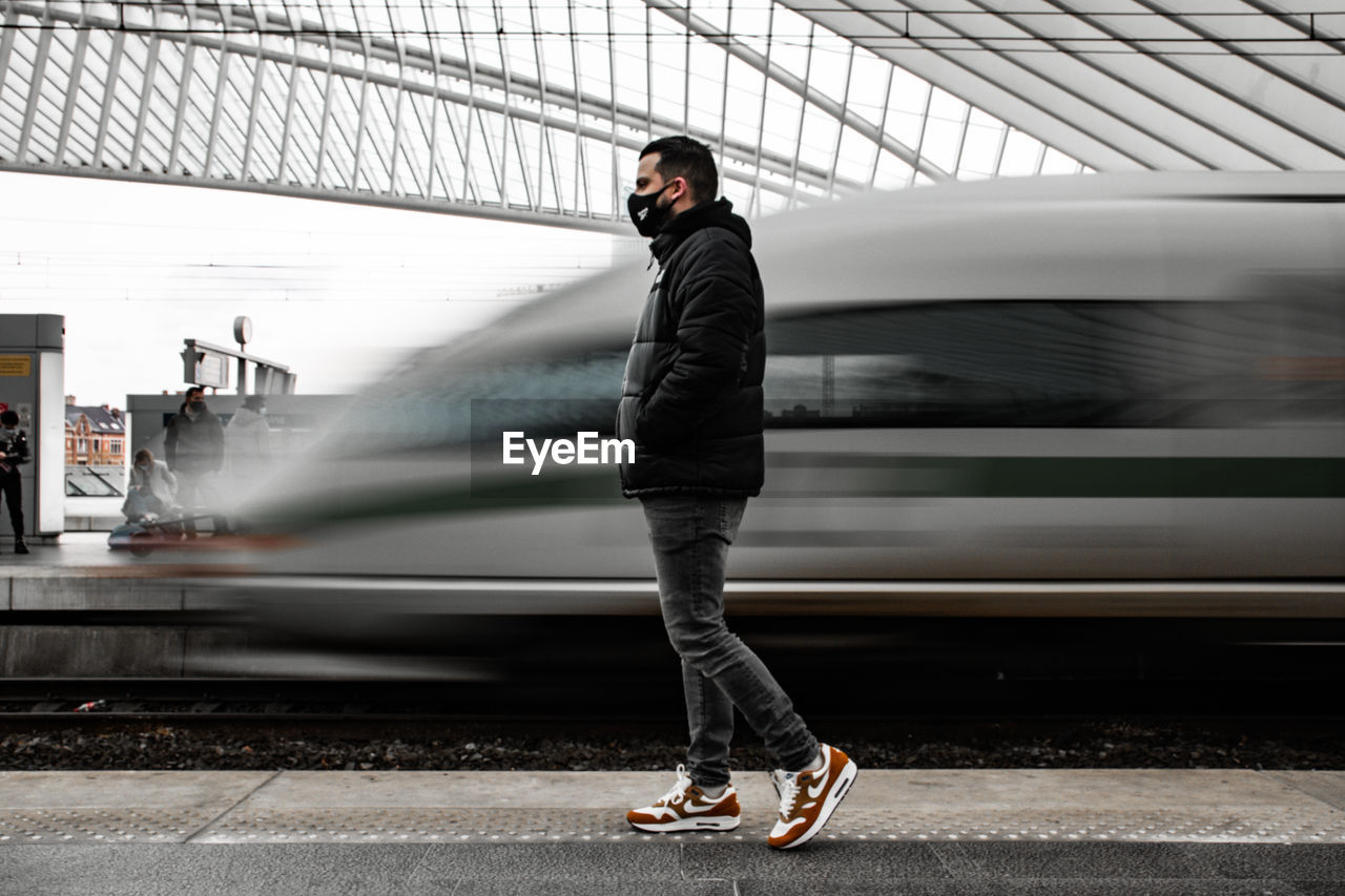 FULL LENGTH OF MAN STANDING ON TRAIN AT RAILROAD STATION