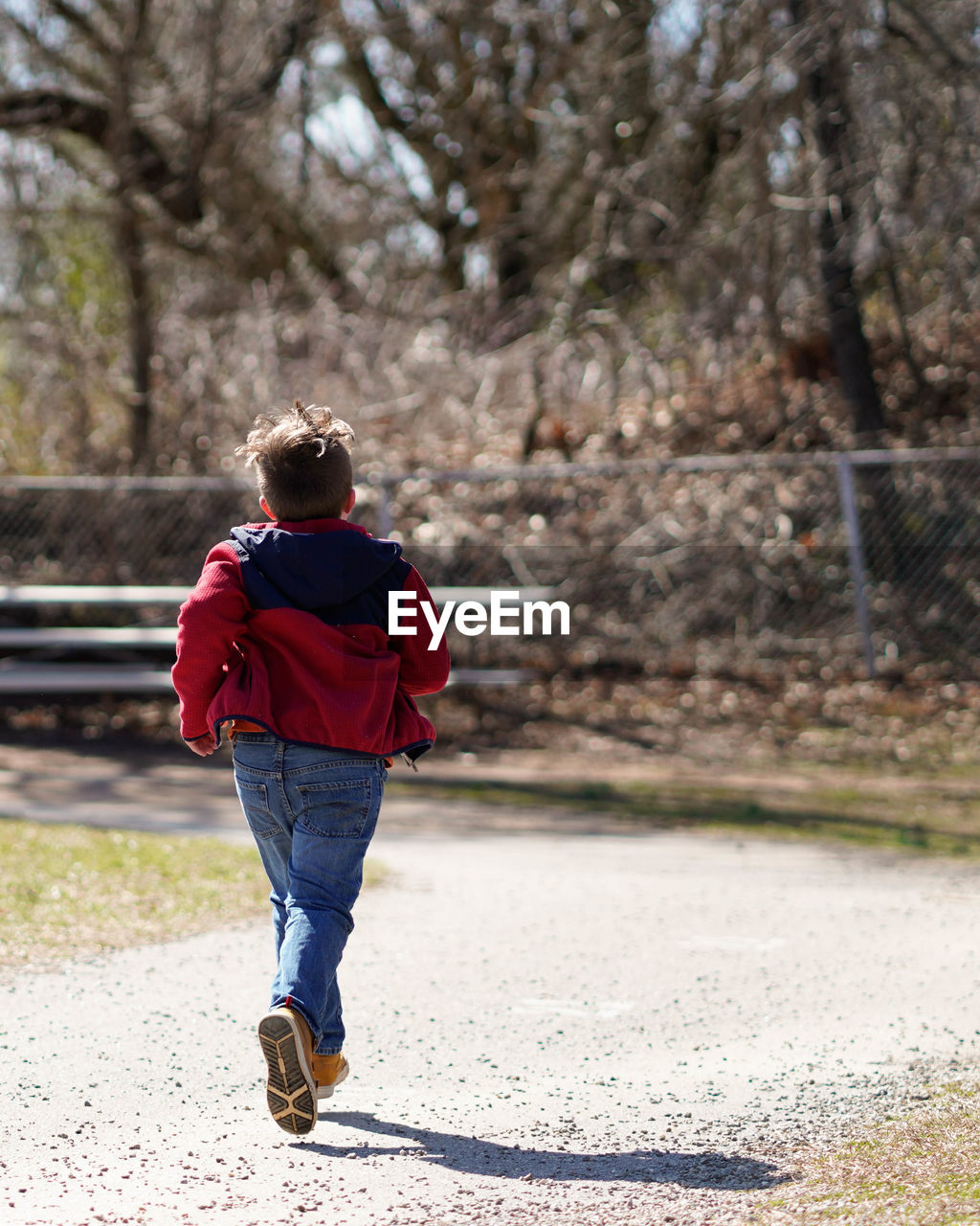 Rear view of boy running on footpath against trees