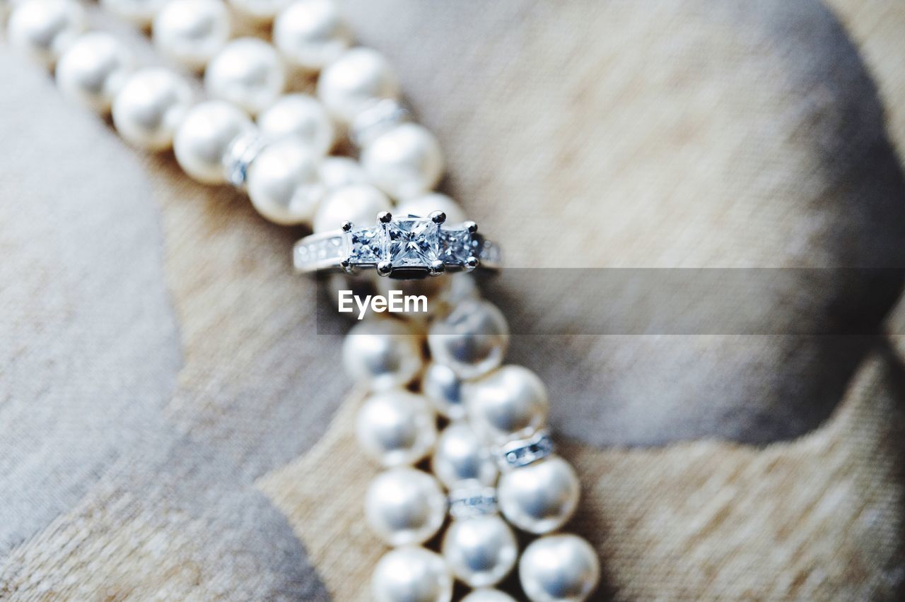 Close-up of engagement ring and pearl necklace