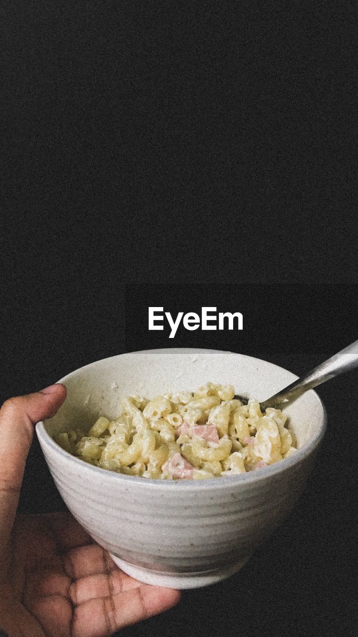 Cropped hand holding bowl with food against black background