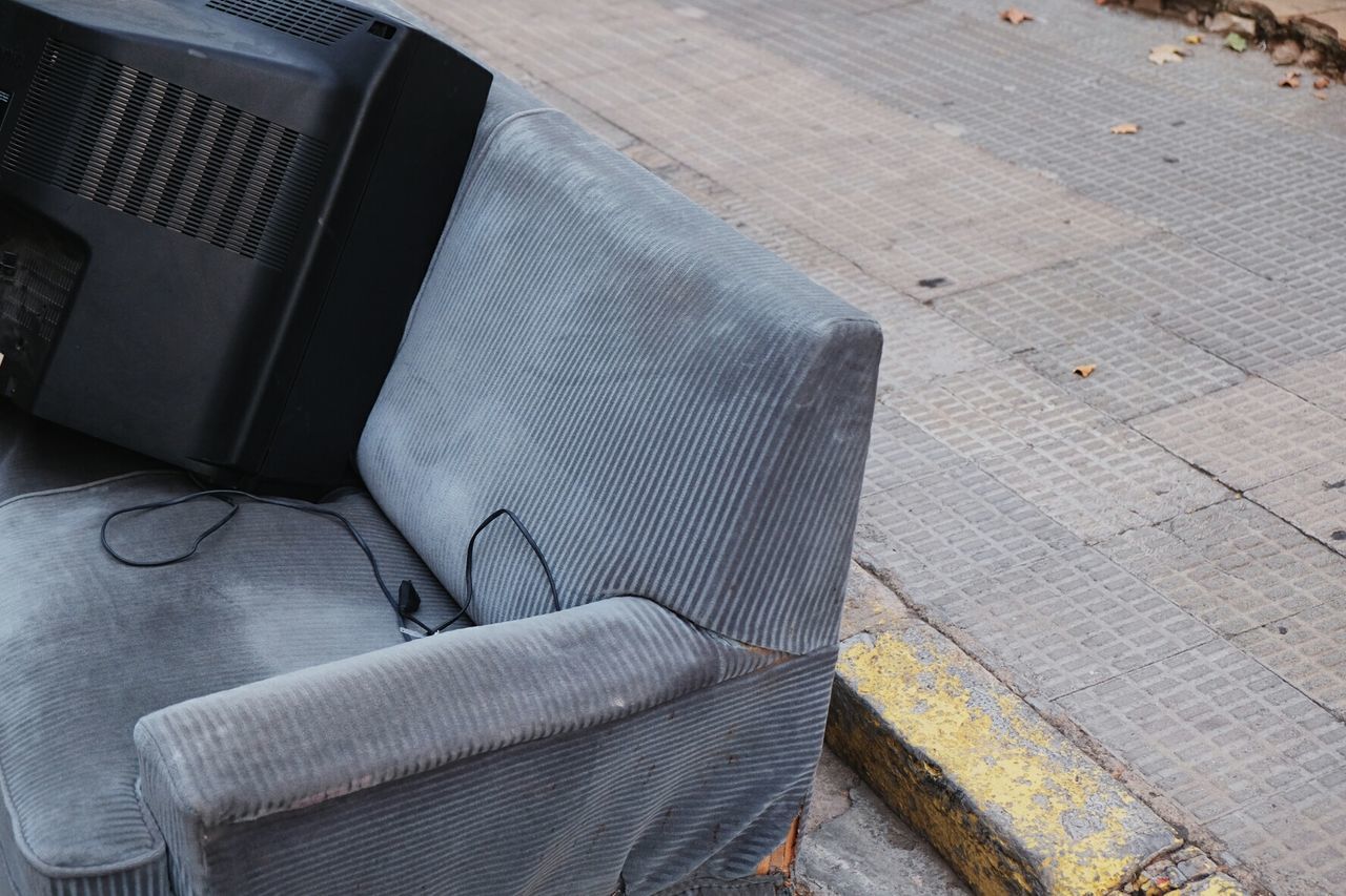 Abandoned television set on sofa against sidewalk