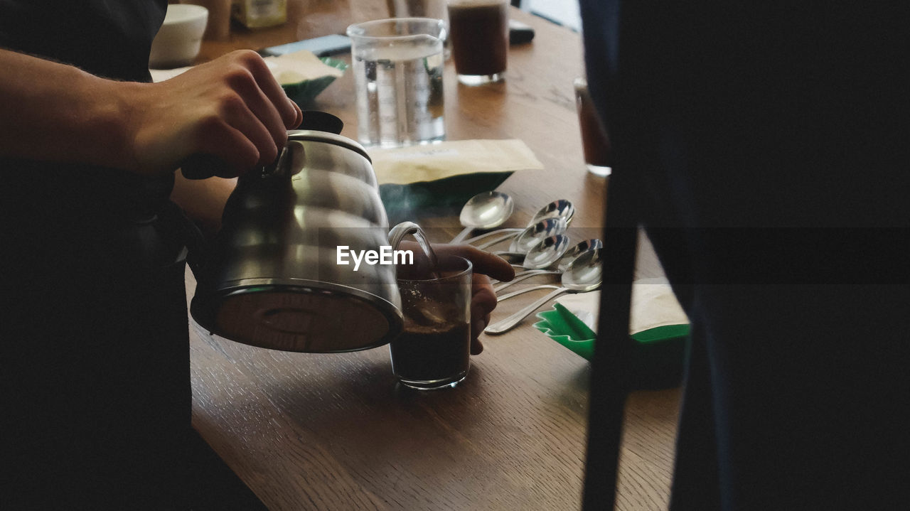 Midsection of man pouring coffee in glass on wooden table