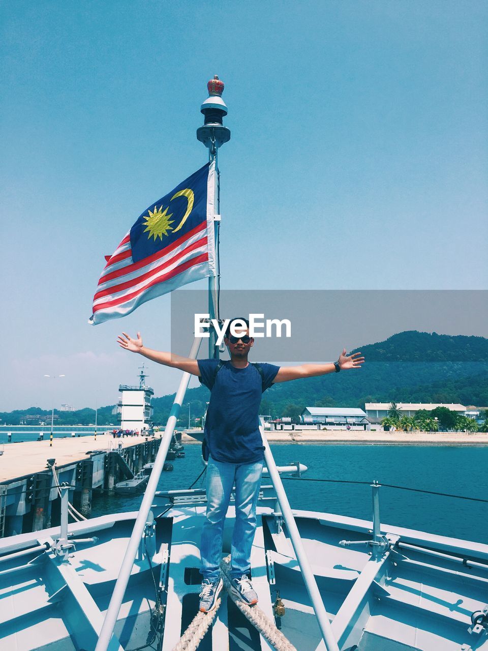 Man with arms outstretched by malaysian flag in boat at sea