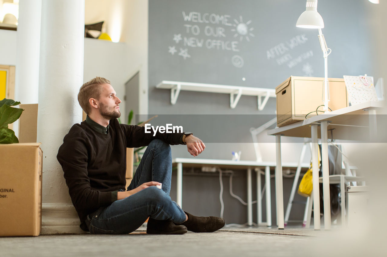 Thoughtful young male entrepreneur sitting on floor at creative office