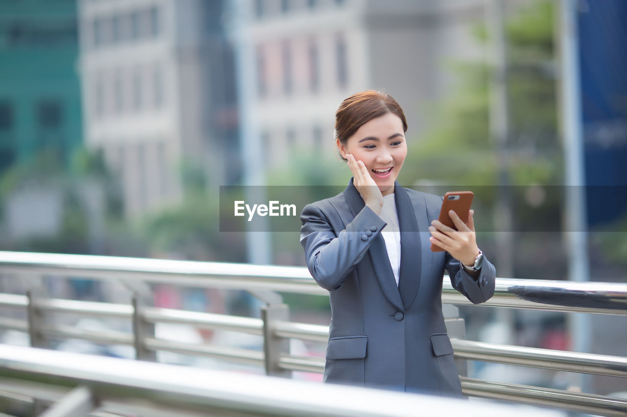 Smiling businesswoman using mobile phone on bridge in city