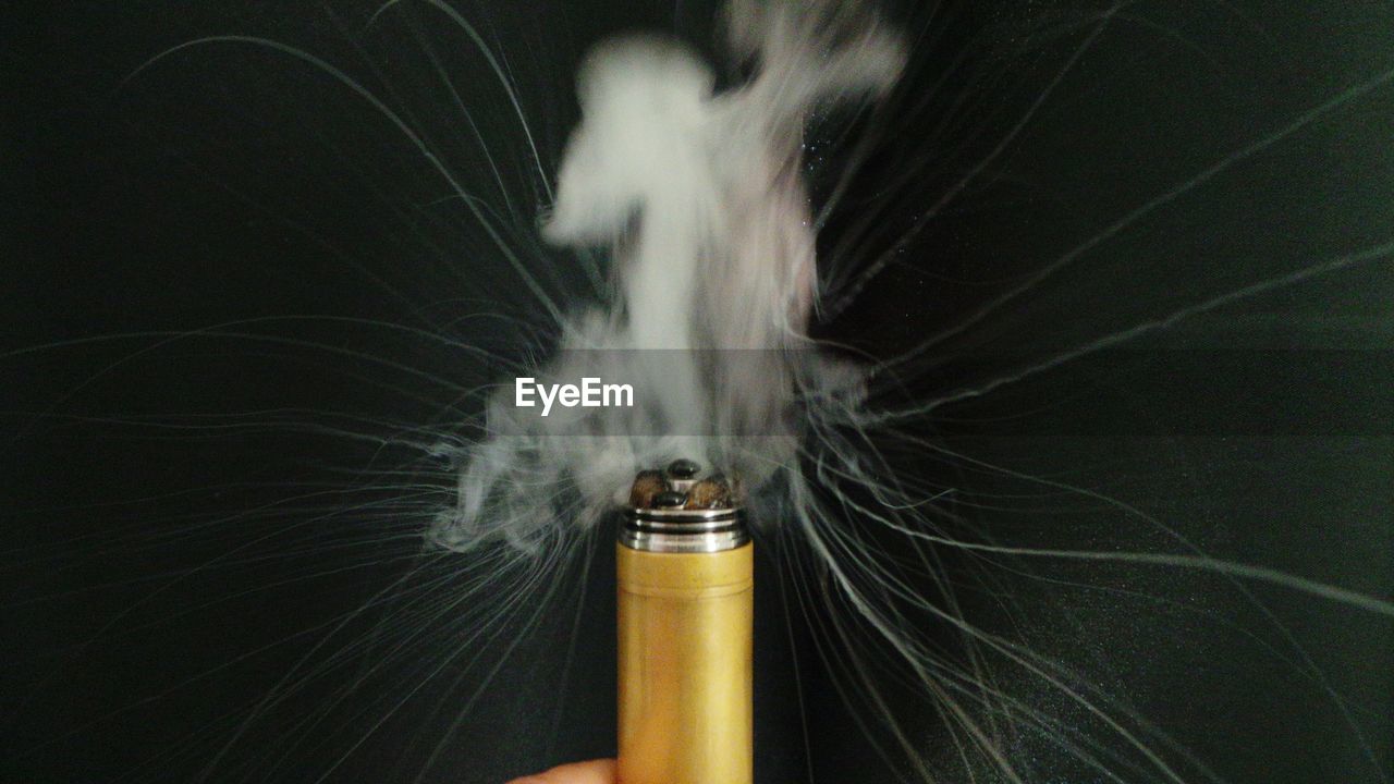 Cropped image of person holding smoke bomb against black background