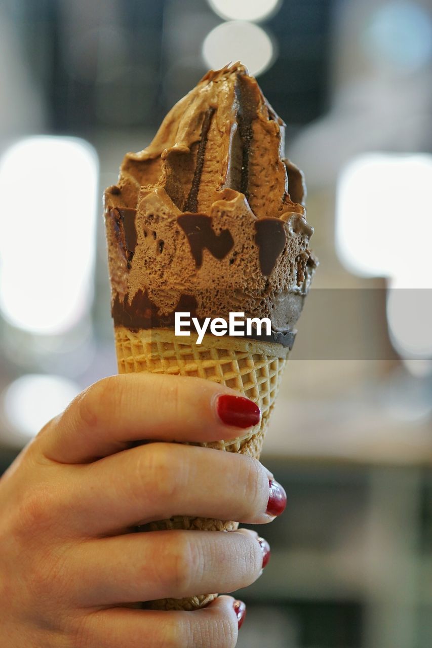 CLOSE-UP OF HAND HOLDING ICE CREAM CONE OUTDOORS