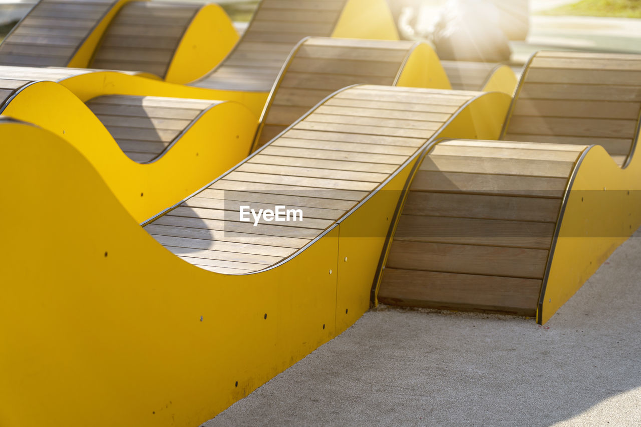 Modern yellow curved wooden benches for relaxing in city park on sunny day. public city resting area