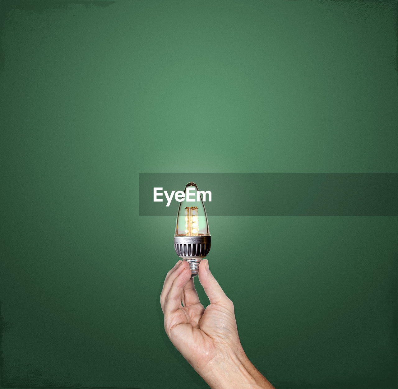 Cropped hand holding light bulb against green background