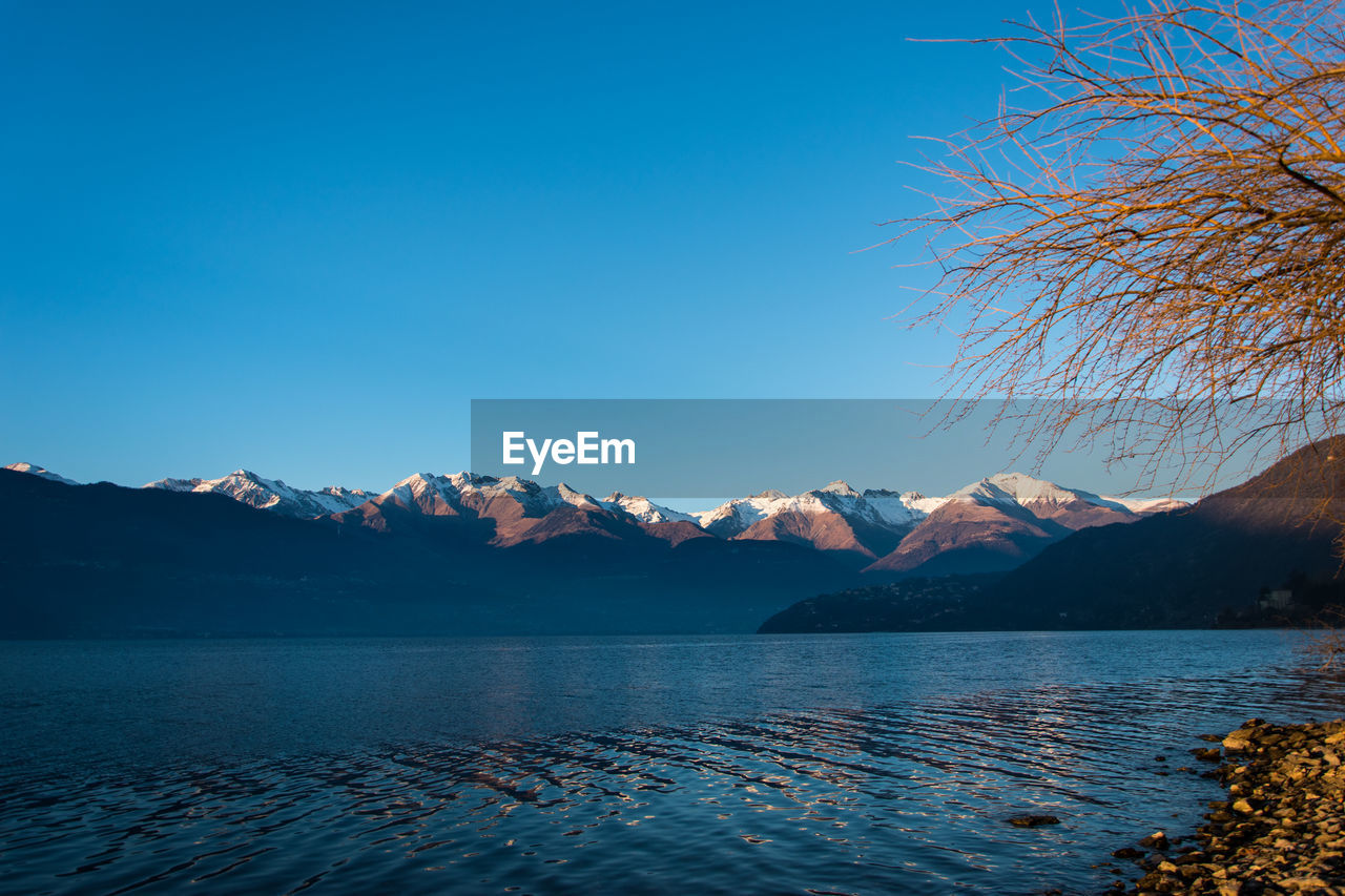 Scenic view of lake and mountains against clear blue sky