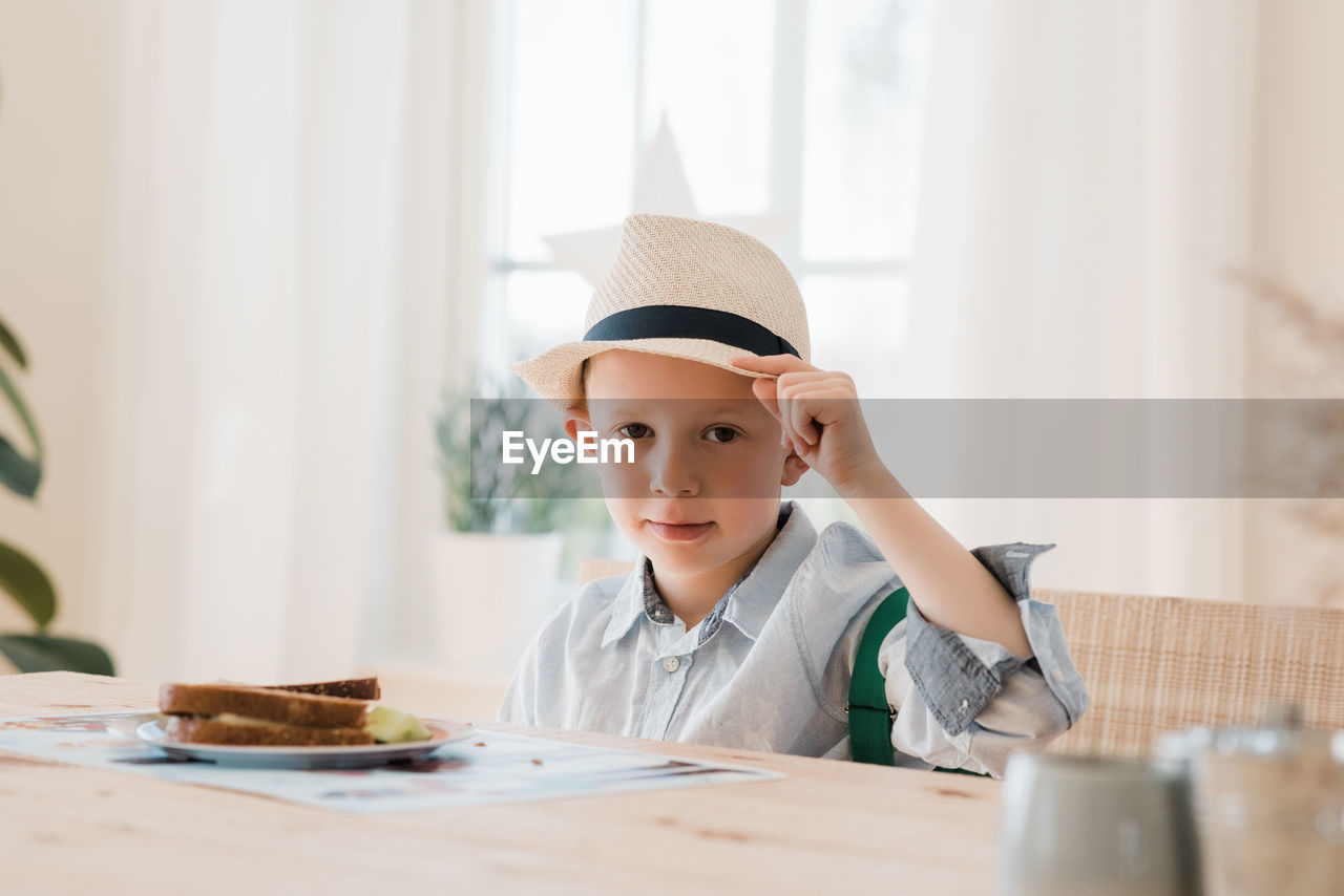 Boy sat eating his breakfast dressed smartly with a hat