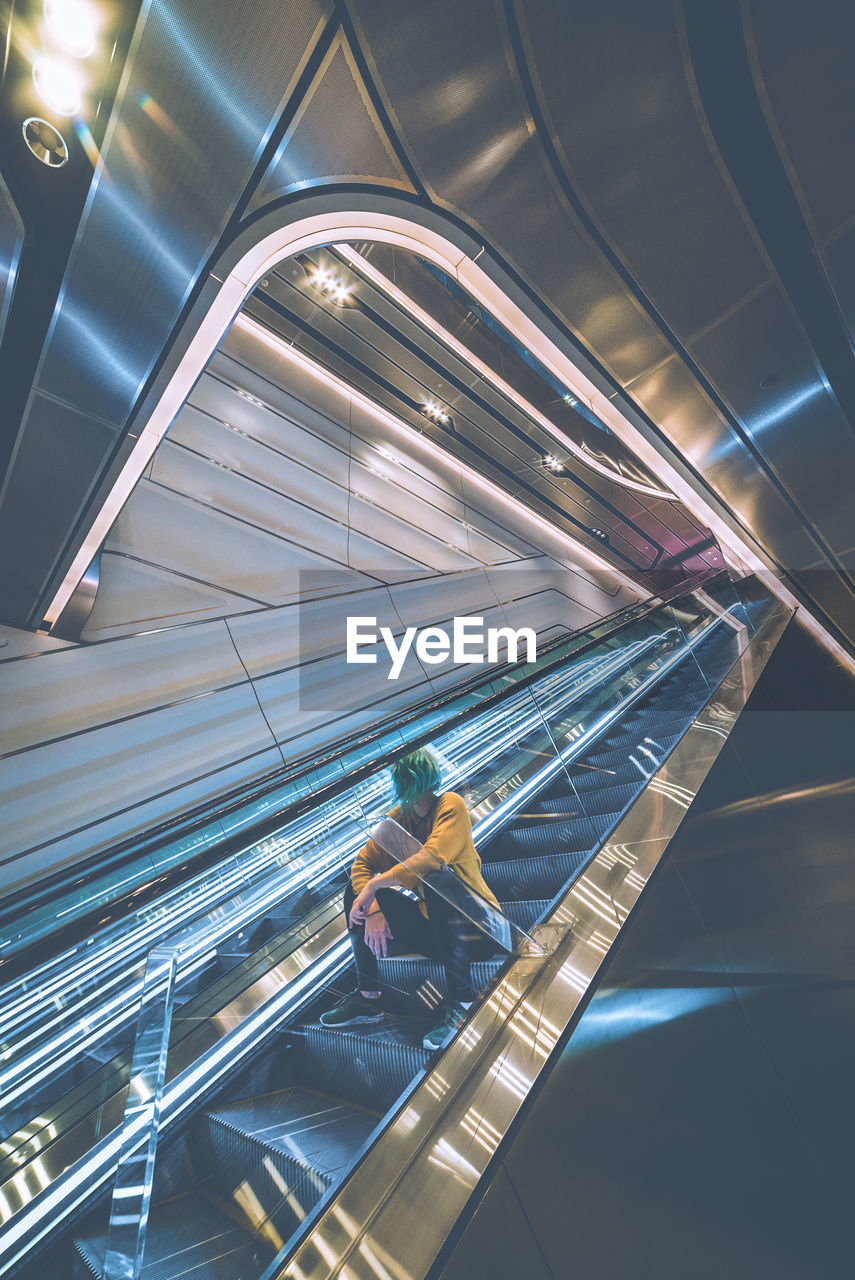 HIGH ANGLE VIEW OF WOMAN SITTING ON ILLUMINATED ESCALATOR