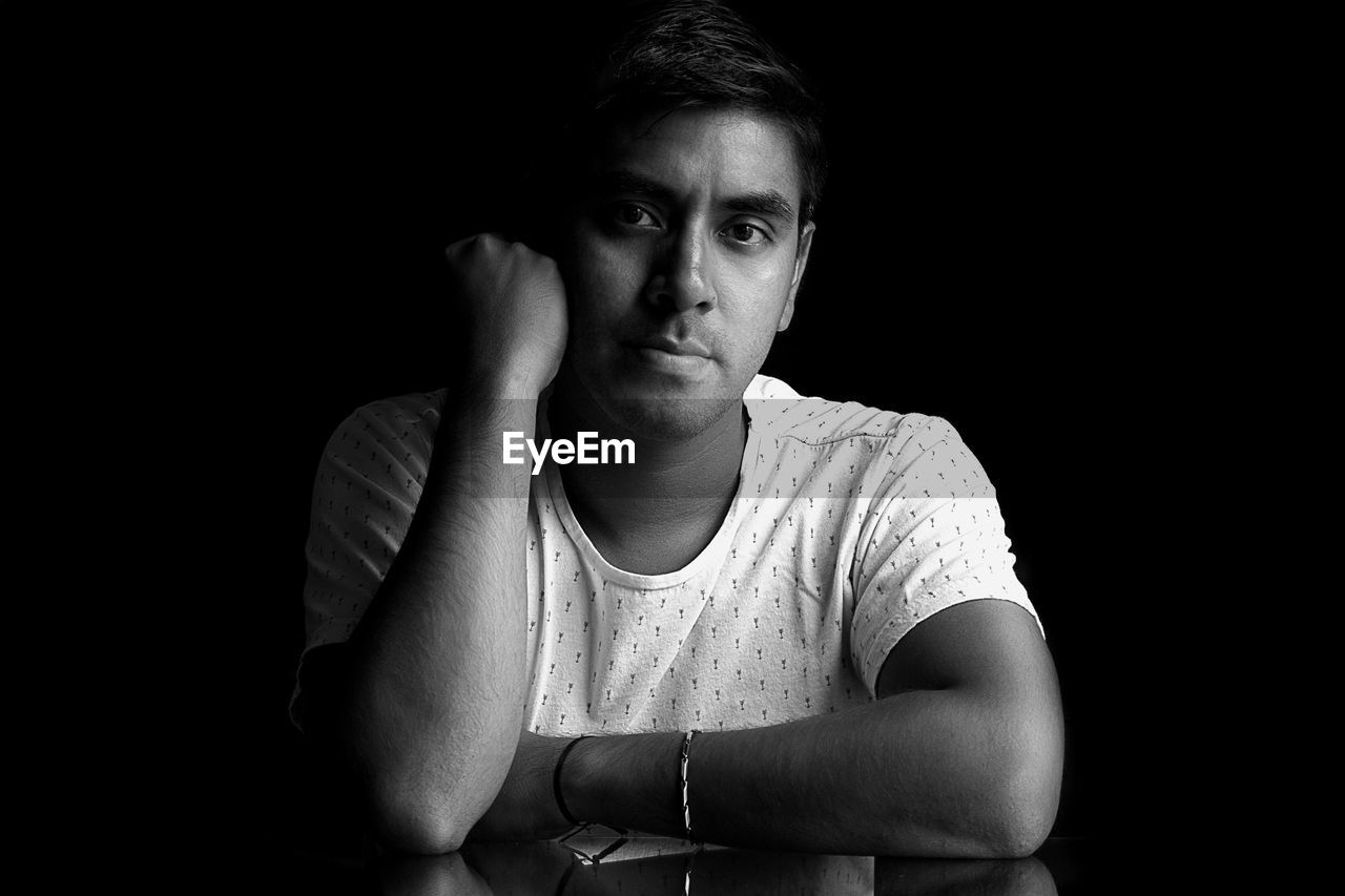 Young man sitting against black background