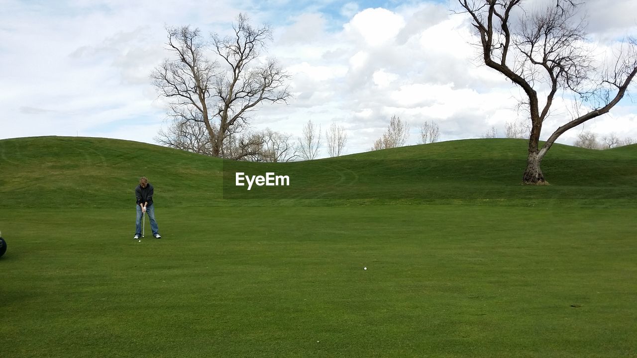 Man playing golf on course against sky