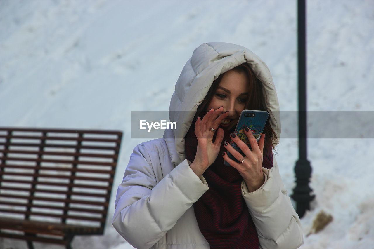 Young woman using mobile phone while standing on snow